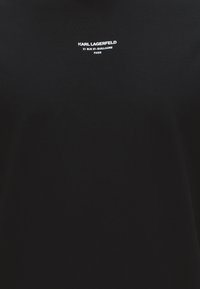 Μαύρο ύφασμα με λευκό κείμενο "KARL LAGERFELD 21 RUE ST-GUILLAUME PARIS" κεντραρισμένο κοντά στην κορυφή.