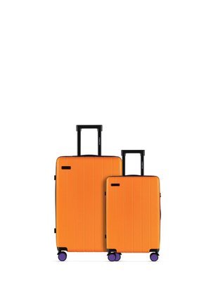 Dwie stojące pionowo pomarańczowe walizki z czarnymi uchwytami i fioletowymi kółkami, jedna duża i jedna średniej wielkości, na białym tle.