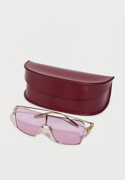 Guccin aurinkolasit, joissa vaaleanpunaiset linssit, kullanvärinen metallikehys ja koristeelliset yksityiskohdat. Mukana viininpunainen nahkakotelo, jossa kohopainettu logo.