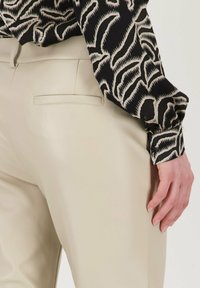 Beige leren broek met een slim fit, met een achterzak. De top heeft een zwart en crème abstract patroon met aansluitende manchetten.