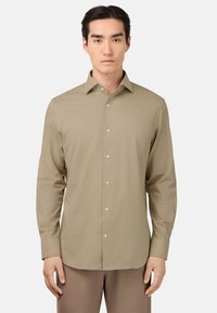 Camisa de manga larga beige con botón frontal, cuello puntiagudo, textura suave y diseño ajustado, combinada con pantalones marrones claros.
