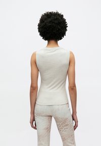 Canotta aderente grigio chiaro con scollo rotondo e design senza maniche, abbinata a pantaloni beige chiaro a fantasia con una trama sottile.