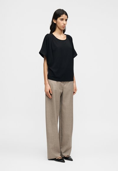 Μαύρο μπλουζάκι με κοντά μανίκια και στρογγυλή λαιμόκοψη, συνδυασμένο με μπεζ παντελόνι φαρδιάς γραμμής και ψηλή μέση, και μαύρα μυτερά φλατ παπούτσια.