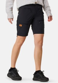 Svarta cargo shorts med flera dragkedjefickor, en tygpatch på vänster lår och uppvikt fåll. Bärs med svarta vandringsskor.