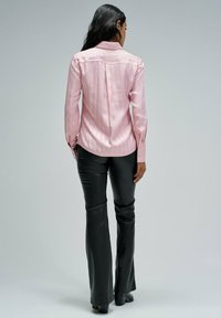 Hellrosa Satinenbluse mit langen Ärmeln und Kragen, die feine vertikale Streifen aufweist, kombiniert mit schwarzen, aus Kunstleder gefertigten, weit geschnittenen Hosen.