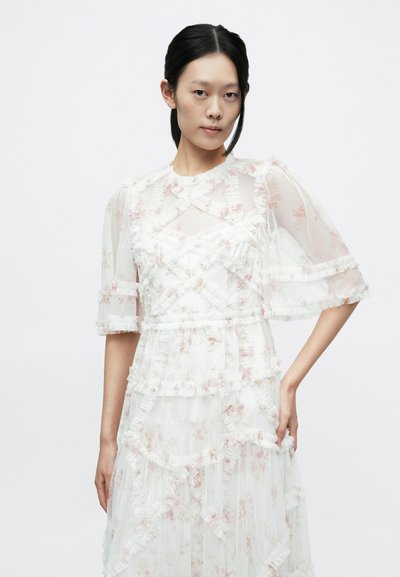 Balta ziedu kleita no caurspīdīga auduma ar volāniem, īsām piedurknēm un kārtainu dizainu ar rozā ziedu rakstiem.