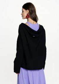 Czarna, oversize bluza z kapturem, z luźnym fasonem i miękką teksturą. Nosi się ją na fioletowej koszulce na ramiączkach, co podkreśla warstwowy styl.