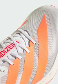 Sports shoe featuring a textured gray upper with orange stripes, white laces, and red branding. Notable 'Lightstrike Pro' detail on the sole.