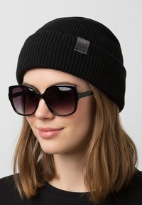 Black ribbed knit beanie with a textured pattern and logo patch, paired with oversized black sunglasses featuring a gradient tint.
