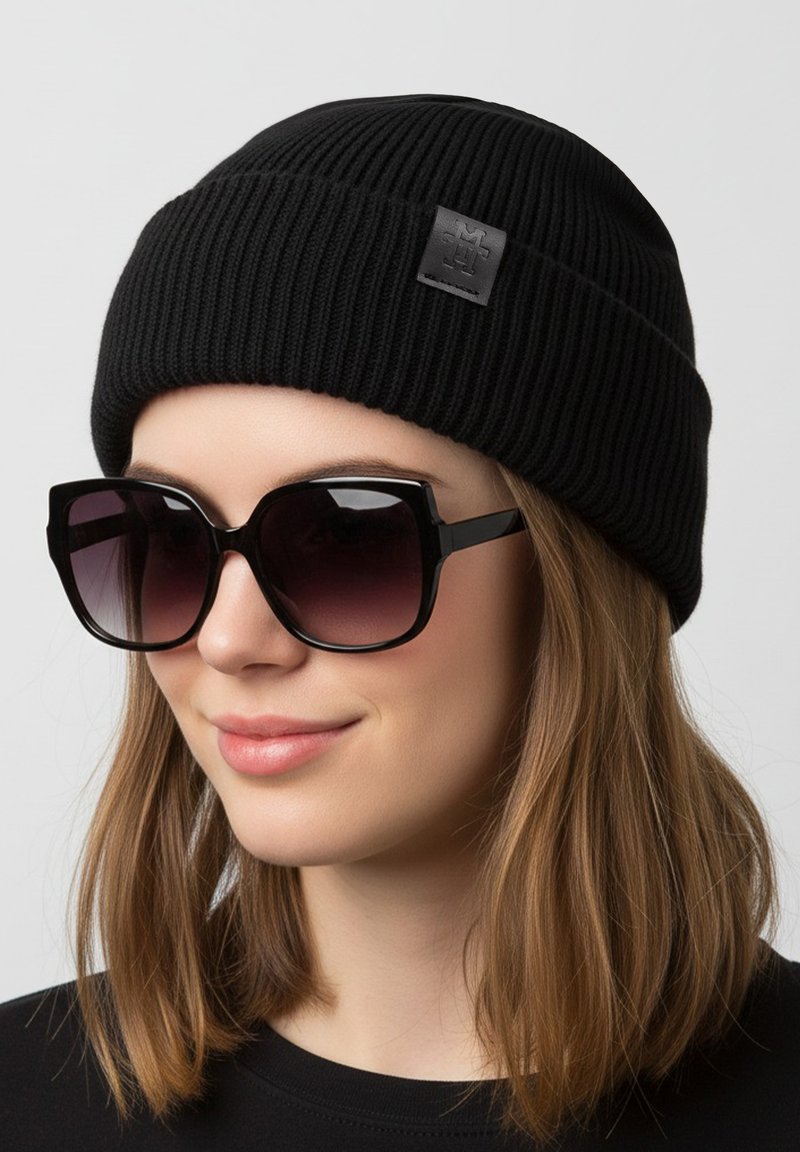 Black ribbed knit beanie with a textured pattern and logo patch, paired with oversized black sunglasses featuring a gradient tint.