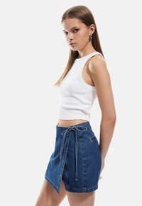 Valkoinen ribatty crop-top, jossa on hihaton muotoilu. Sininen denim-kietaisuhame, jossa on solkityyli, repaleinen helma ja sivutaskut.
