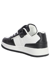 Sneaker bianco e nero con una tomaia in pelle, texture liscia, suola in gomma, cinturino regolabile e dettagli di cucitura a contrasto.