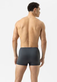 Dark gray swim trunks with a textured surface, featuring a fitted design and an elastic waistband. The fabric has a subtle pattern.