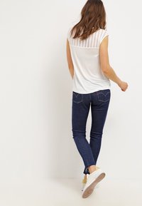 Vit kortärmad topp med meshrygg, tillsammans med mörkblå skinny jeans och vita sneakers med gula accenter.