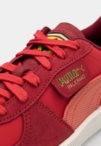 Baskets en daim rouge et synthétique avec des lacets texturés, logo doré et accents de panneaux. Présente une semelle distincte et un col rembourré.