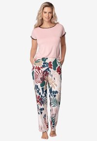 Różowa bluzka z krótkim rękawem z czarnymi wykończeniami; jasne spodnie w kwiatowy wzór w kolorach czerwonym, zielonym i beżowym z kieszeniami, wykonane z miękkiego materiału.