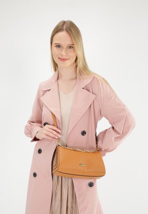 Tan læder skuldertaske med struktureret overflade, sort kant og guldkæde-rem. Modellen har en lys pink trench coat på over en nude top.