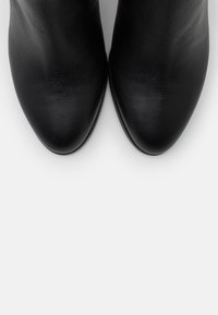 Bottes cheville en cuir noir à texture lisse, bouts pointus et silhouette fine. Présentent un motif de grain subtil sur l'ensemble.