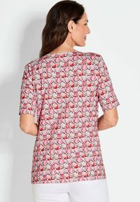 Kurzärmliges Oberteil mit einem rosa Hintergrund und einem wiederholten Muster aus roten und weißen Formen. Hergestellt aus einem leichten, strukturierten Stoff.