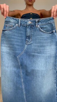 Personne portant un haut sans bretelles tenant un jean en denim bleu surdimensionné, étiré largement devant elle.