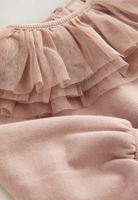 Vêtement rose clair avec un col en tulle volanté et un tissu doux. La texture est lisse avec des détails froncés au niveau des manches.