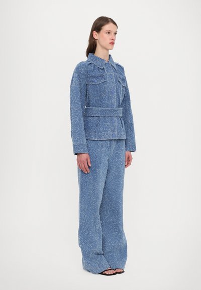 Set de jachetă și pantaloni texturat albastru, cu talie prinsă în curea, două buzunare pe piept și picioare largi. Țesătură netedă cu un model pârjit.