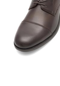 Brūnas ādas kleitu kurpes ar noapaļotu purngalu, šūtām akcentiem un auklu dizainu. Gluda tekstūra ar spīdīgu apdari.