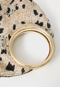 Gold circular bangle on a textured, beige fabric with black animal print. The bangle features a smooth, shiny surface with layered design.
