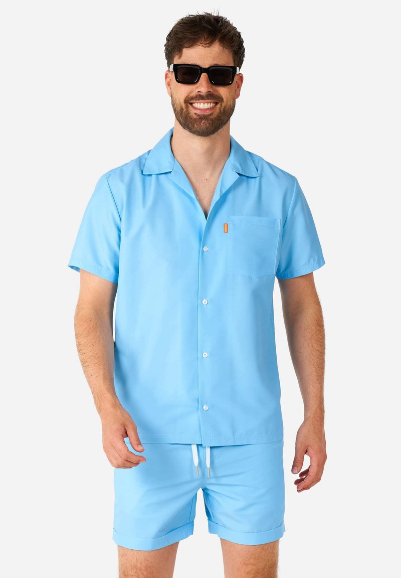 Camicia azzurra a maniche corte con bottoni, dotata di una tasca sul petto, abbinata a pantaloni corti blue coordinati con cintura elastica e stringa.