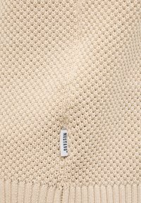Beige gestrickter Pullover mit strukturierten Mustern, geripptem Saum und einem kleinen Etikett mit "MUSTANG" an der Seite.