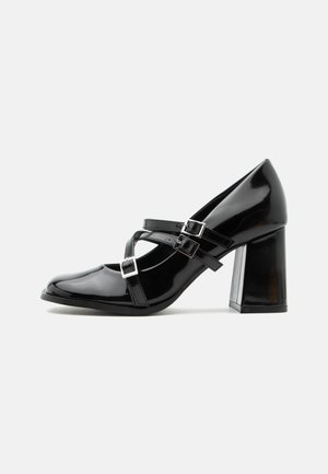 Zapato de tacón alto estilo Mary Jane negro brillante con tres tiras con hebillas y un tacón de bloque grueso, mostrado de perfil sobre fondo blanco.