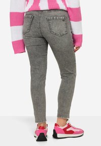Jeans ajustados grises con un acabado texturizado, cintura de altura media y dos bolsillos traseros, combinados con zapatillas de deporte en rosa y blanco en bloque de color.