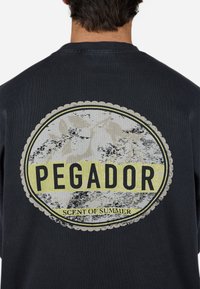 Sort sweatshirt med et stort cirkulært grafik på ryggen. Designet inkluderer "PEGADOR" i fed skrift og en tagline "Scent of Summer", med blomsteraccenter.