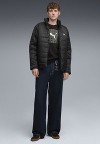 Chaqueta de plumas negra, camiseta de manga larga negra con gráfico gris, vaqueros oscuros anchos, zapatos negros con suela de goma, llavero en la mano derecha.