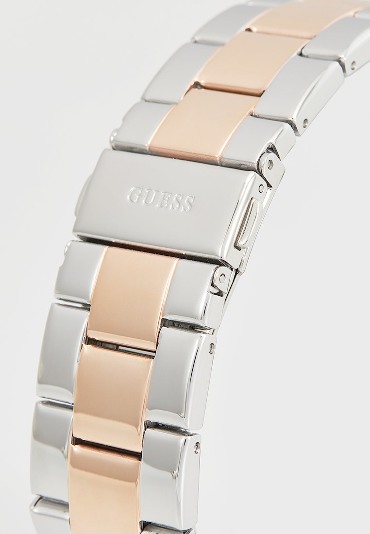 Bracciale in acciaio inossidabile con maglie alternate in argento e oro rosa, dotato di una chiusura contrassegnata con "GUESS." Finitura liscia e lucida.