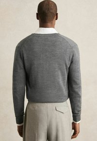 Gray sweater with a crew neckline, ribbed cuffs, and a smooth texture, worn over a white collared shirt and paired with light gray trousers.