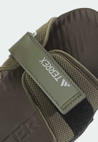 Sandał w kolorze oliwkowej zieleni z teksturowanym, siateczkowym wierzchem, regulowanym paskiem z białym logo oraz gumową podeszwą z poziomymi rowkami.