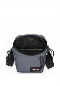 Harmaa Eastpak olkalaukku, jossa on vetoketjulla avattava yläosa, musta vuoraus sisäpuolella, säädettävä olkahihna ja logopatch edessä.