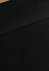 Tessuto a coste nero con una cintura liscia e una trama decorata, caratterizzato da dettagli di cucitura e un colore uniforme.