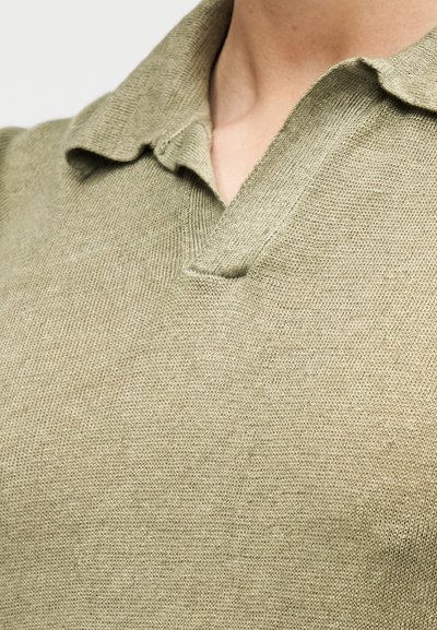 Polo tricoté en vert olive discret avec un col court et un décolleté en V, fabriqué dans un tissu doux et texturé.