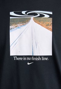 Svart t-skjorte med et grafisk design av en vei omgitt av gress, med et spiraldesign ovenfor og teksten "Det finnes ingen målgang." i hvitt.