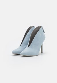 Bottines en daim bleu clair avec un bout pointu, des côtés ouverts et un fin talon haut. Intérieur doublé de tissu gris au toucher lisse.