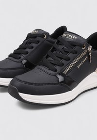 Sneaker nera con tomaia in pelle liscia, lacci, dettagli con zip laterale e intersuola bianca. Presenta una punta rotonda e accenti testurizzati.