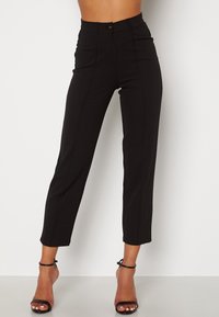 Pantalon noir sur mesure taille haute, avec fermeture à bouton, jambes droites, et texture lisse. Longueur cheville sans motifs visibles.