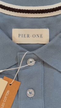 Polo shirt azzurro chiaro in cotone testurizzato, con colletto a strisce bianche e marroni, due bottoni e un'etichetta in tessuto con la scritta "PIER ONE."
