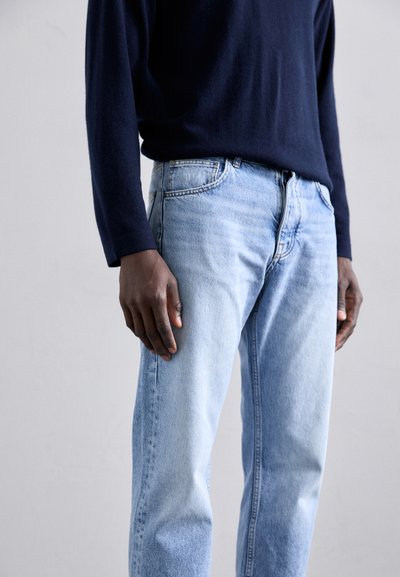 Lyseblå jeans med avslappet passform, fem-lommers design og falmet tekstur, sammen med en mørk marineblå genser med lange ermer.