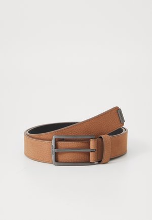 Ceinture en cuir marron avec boucle en métal foncé, pliée, logo Calvin Klein sur la boucle et l'extrémité de la ceinture sur fond uni.
