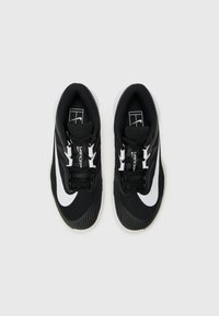 Sorte træningssko med en struktureret overdel, hvid swoosh-logo og sorte snørebånd. Sålen er hvid med et rillet mønster for bedre greb.