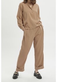 Beige, letvægts, langærmet bluse med knaplukning, parret med løstsiddende, manchetter på beige bukser og sorte loafers med guld detaljer.