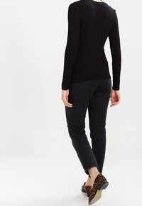 Schwarzes Langarmshirt kombiniert mit schwarzen Jeans. Das Outfit zeichnet sich durch ein figurnahes Design und flache Schuhe mit Leopardenmuster und strukturiertem Oberflächen aus.
